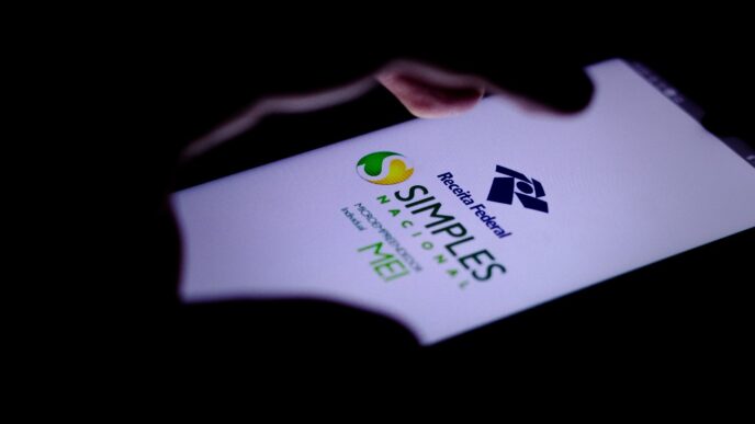 Pessoa com smartphone na mão e o sistema do Simples Nacional na tela